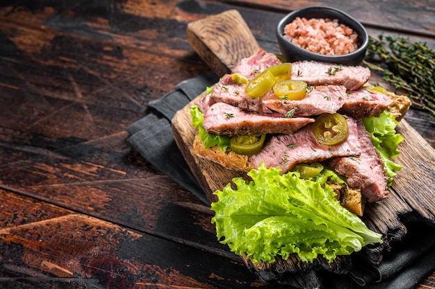 Sándwich de bistec con ensalada de ternera a la parrilla en rodajas y verduras en pan Fondo de madera Vista superior Espacio de copia