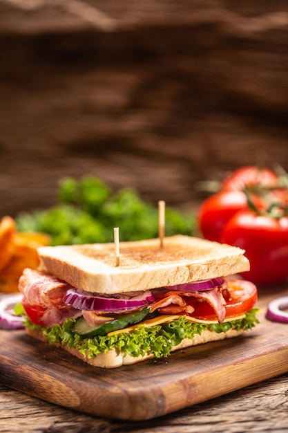 Sándwich BLT con cebolla sobre una tabla de cortar con un fondo oscuro.