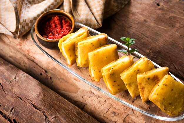 Sandwich Bread Pakora oder Pakoda (Dreiecksform) serviert mit Tomatenketchup, Chutney, grünen Chili- und Zwiebelscheiben, beliebter indischer Snack zur Teezeit. Selektiver Fokus