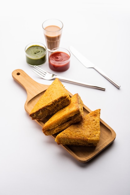 Sandwich Bread Pakora oder Pakoda in Dreiecksform, serviert mit Tomatenketchup, grünem Chutney, beliebter indischer Snack zur Teezeit