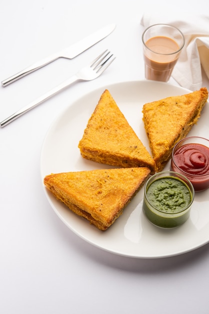 Sandwich Bread Pakora oder Pakoda in Dreiecksform, serviert mit Tomatenketchup, grünem Chutney, beliebter indischer Snack zur Teezeit