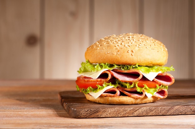 Sandwich-Burger mit Schinken, Käse und Gemüse auf einem rustikalen TablexA