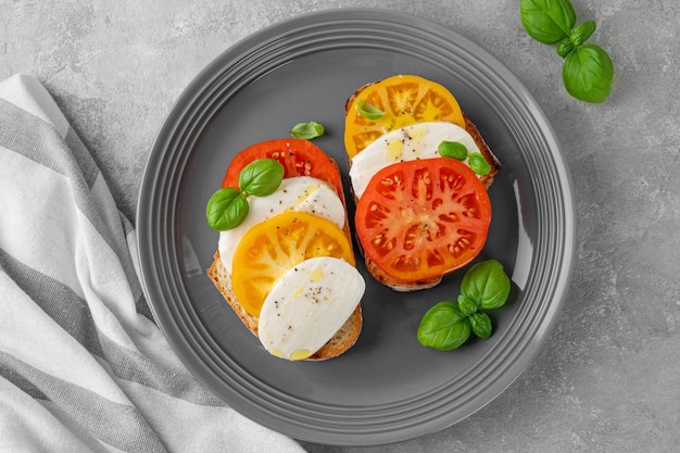 Foto sandwich caprese mit roggenbrot, tomaten, mozzarella und frischem basilikum auf einem grauen teller gesundes essen