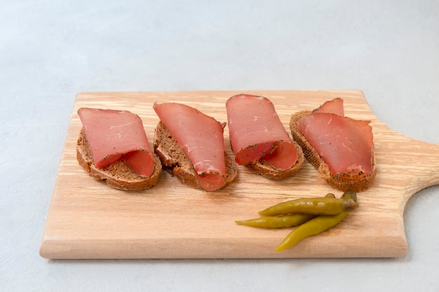Sándwich con carne seca en rodajas servida sobre tabla de cortar sobre fondo gris neutro
