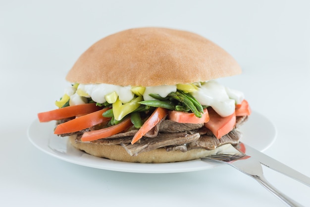 Sándwich de carne con tomate, judías verdes, chile y mayonesa con fondo blanco