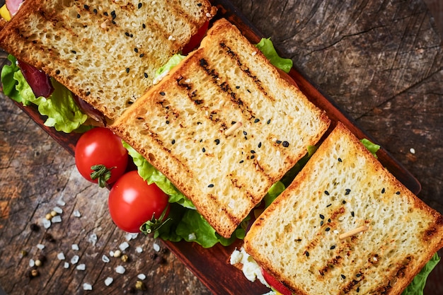 Sandwich casero con jamón, lechuga, queso y tomate sobre un fondo de madera, vista superior