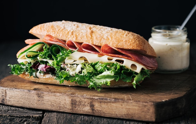 Sándwich casero con queso de jamón y hojas de lechuga sobre fondo de madera oscura enfoque selectivo