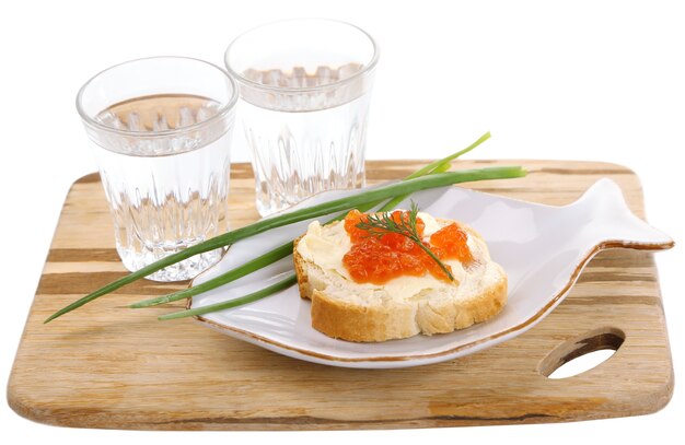 Sándwich con caviar y vodka en tablero de madera aislado en blanco