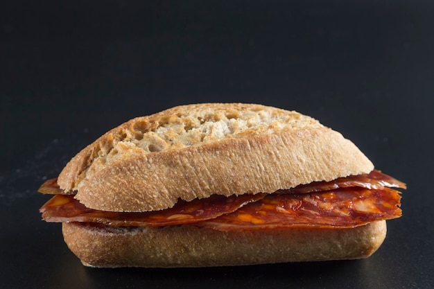 Foto sándwich de chorizo sobre un fondo negro pan crujiente y rebanadas de salchicha roja