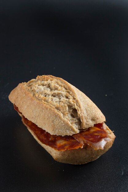 Foto sándwich de chorizo sobre un fondo negro pan crujiente y rebanadas de salchicha roja