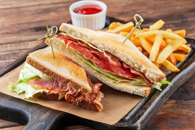 Sándwich club sobre una tabla de madera Junto a papas fritas y una taza de salsa de ketchup