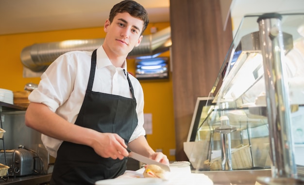 Sándwich de corte trabajador masculino en el mostrador