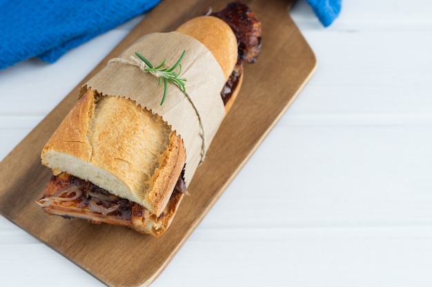 Sandwich de costilla en salsa de barbacoa sobre una base de madera blanca