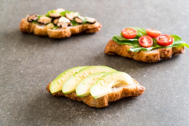 Sándwich de croissant con aguacate, tomate y champiñones.