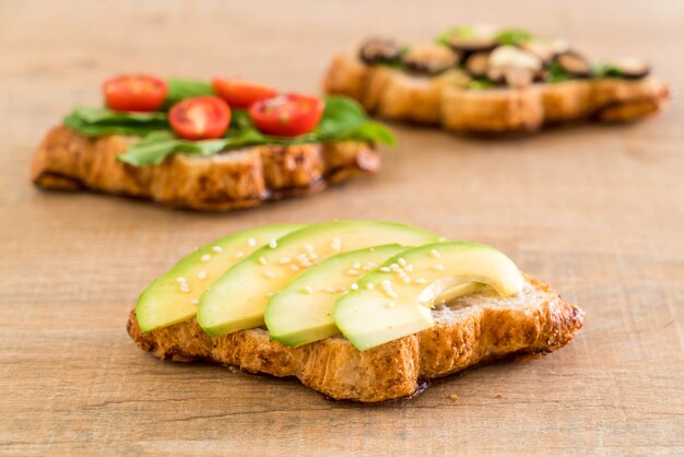 Sándwich de croissant con aguacate, tomate y champiñones.