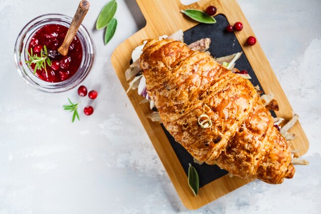 Sandwich de croissant con carne de pato, queso crema y salsa de arándanos en el tablero