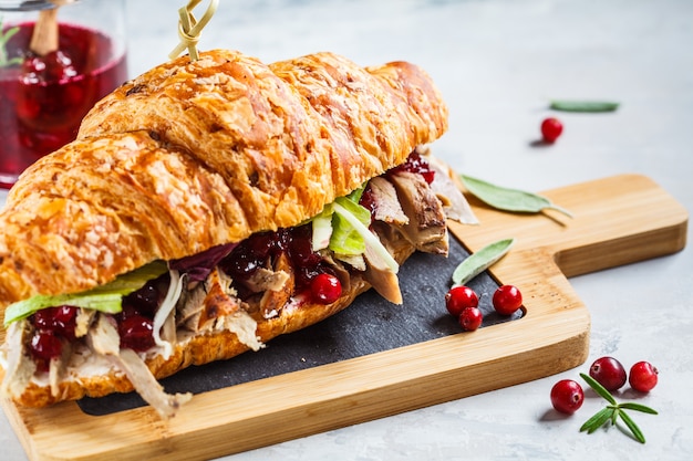 Sandwich de croissant con carne de pato, queso crema y salsa de arándanos en el tablero