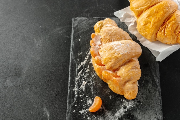 Sándwich de croissant dulce con mandarinas en el espacio de copia de fondo oscuro