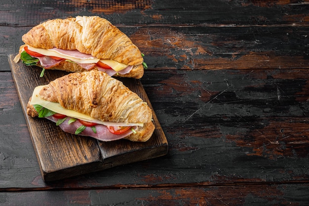 Sándwich de croissant fresco con jamón, queso y ensalada de hojas, sobre fondo de mesa de madera oscura, con espacio para copiar texto