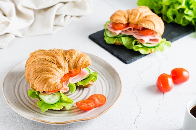 Sándwich de croissant con jamón, pepinos, tomate y lechuga en un plato sobre la mesa