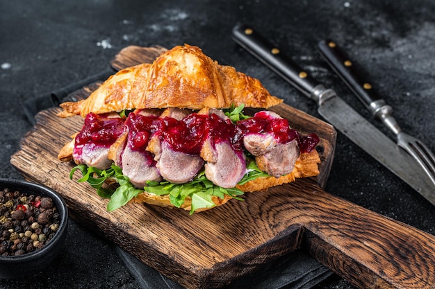 Sándwich de croissant con lonchas de filete de pechuga de pato, rúcula y salsa. Fondo negro. Vista superior.