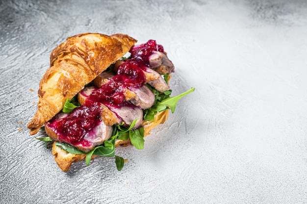 Sándwich de croissant de pechuga de pato con rodajas de bife, rúcula y salsa. Fondo blanco. Vista superior. Copie el espacio.