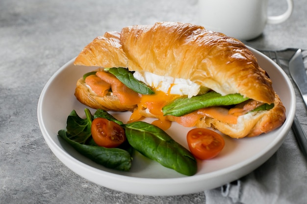 Sándwich de croissant con requesón, salmón, espinacas y huevo escalfado en un plato