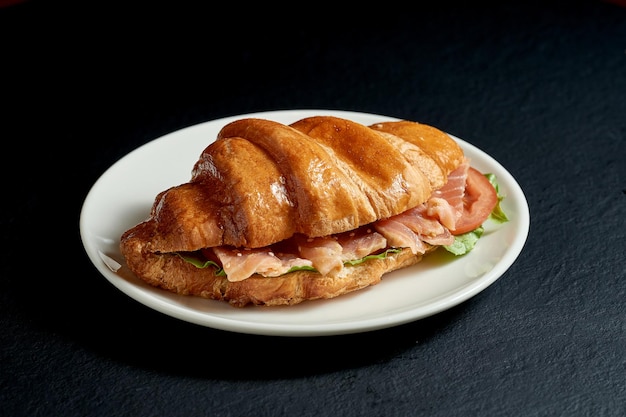 Sándwich de croissant con salmón en un plato blanco sobre fondo negro