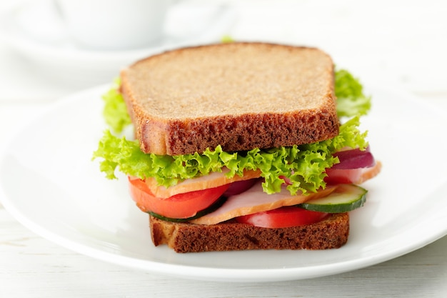 Sándwich delicioso y saludable con jamón, lechuga, tomate y cebolla y pepino en un plato