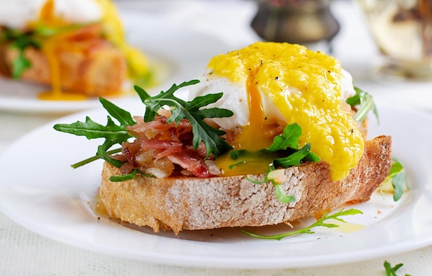 Sandwich de desayuno con jamón, cebolla de huevo pocheado y rúcula en un plato sobre un fondo claro