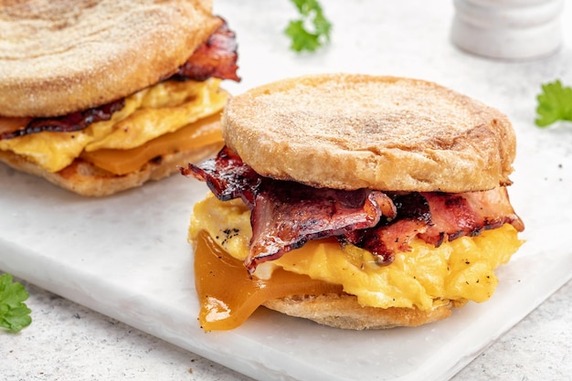 Sándwich de desayuno de jamón y queso con huevo de muffin inglés en una tabla para cortar