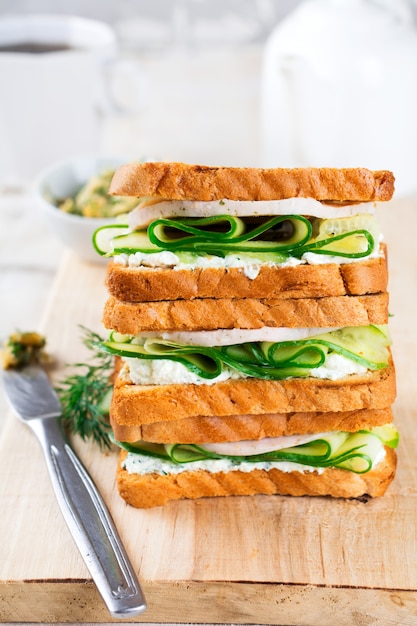 Sandwich para el desayuno relleno de rodajas de pepino, requesón, jamón y eneldo sobre fondo de madera vieja. Enfoque selectivo.