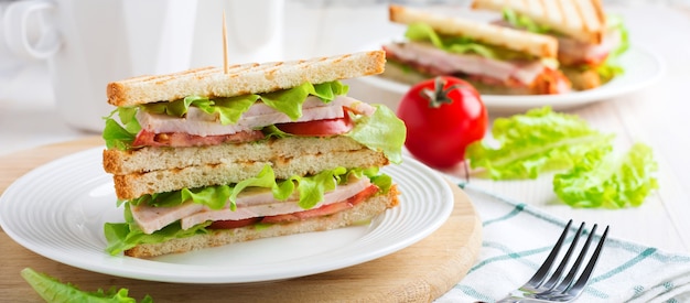 Sándwich de desayuno con tomates rellenos de jamón y lechuga sobre un fondo de madera clara. Enfoque selectivo.