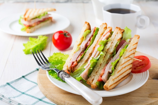 Sándwich de desayuno con tomates rellenos de jamón y lechuga sobre una superficie de madera clara. Enfoque selectivo.