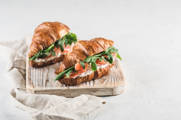 Sándwich de dos croissants con salmón, queso ricotta y rúcula sobre una tabla de madera con una servilleta