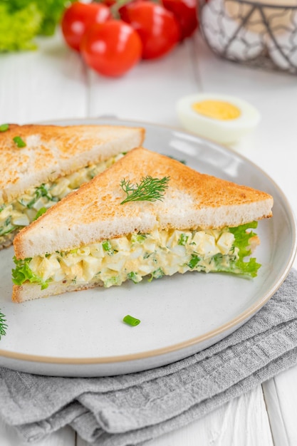 Sándwich de ensalada de huevo con pan tostado y lechuga sobre un fondo de madera blanca El enfoque selectivo