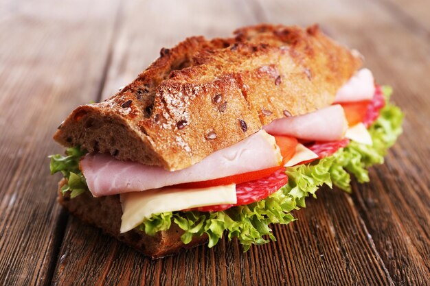 Sándwich fresco y sabroso con jamón y verduras sobre fondo de madera