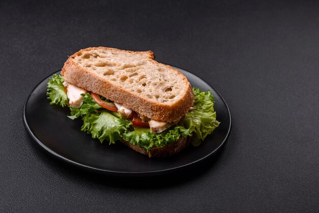 Foto sándwich fresco y sabroso con tomates de pollo y lechuga en un plato negro