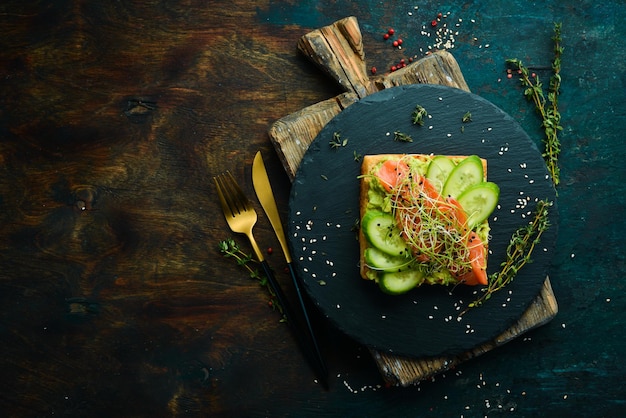 Sandwich. Frisches Stück Ciabatta mit Avocado-Hummus und gesalzenem rotem Fisch. Auf einer schwarzen Steinplatte.