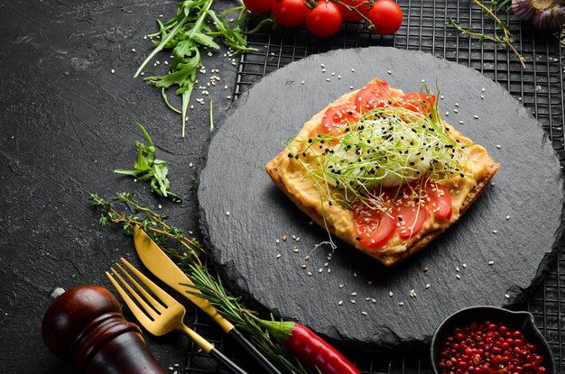 Sandwich Frisches Stück Ciabatta mit Hummus-Tomaten und Ei Frühstück auf einer schwarzen Steinplatte