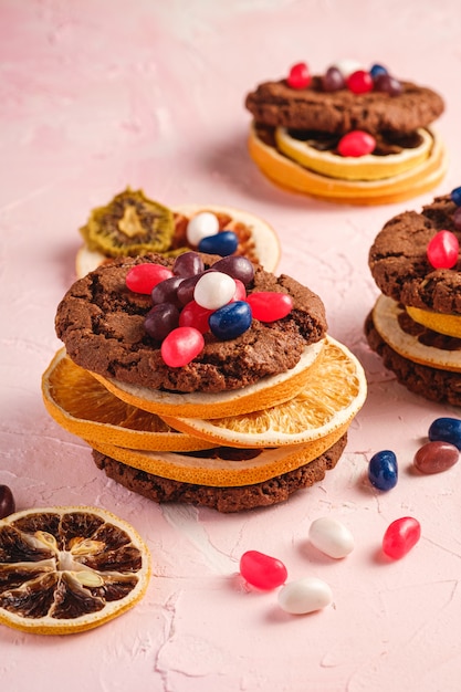 Foto sandwich de galletas de chocolate de avena caseras con cítricos secos y jugosas gominolas sobre fondo rosa con textura, vista de ángulo