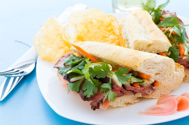 Sándwich gourmet banh-mi con patatas fritas a un lado.