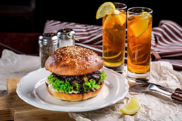 Sándwich de hamburguesa de pollo, tomate, queso y lechuga. Burger está sobre la mesa con papel y salero y pimentero. Además de dos cócteles, Log Island Iced