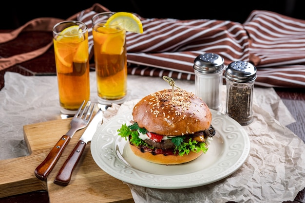 Sándwich de hamburguesa de pollo, tomate, queso y lechuga. Burger está sobre la mesa con papel y salero y pimentero. Además de dos cócteles, Log Island Iced