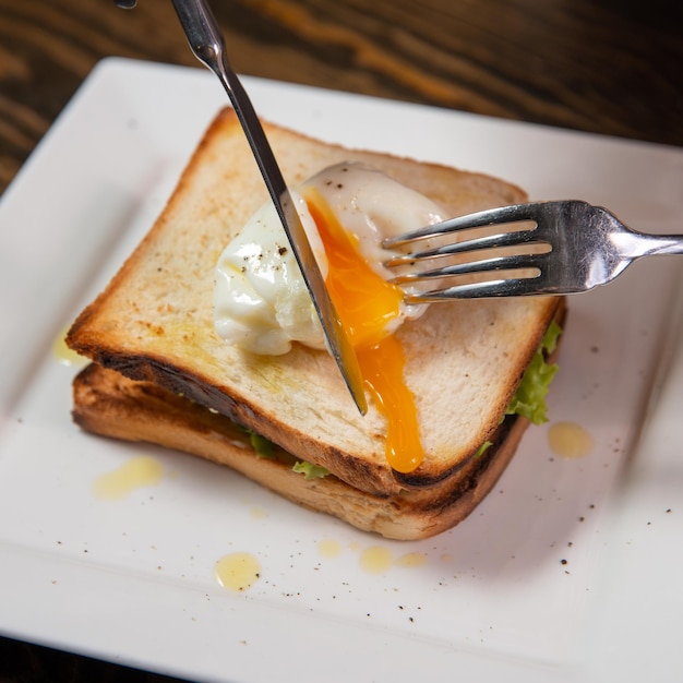 Sándwich con huevo escalfado y jamón aislado en un espacio de copia de mesa de madera de cerca