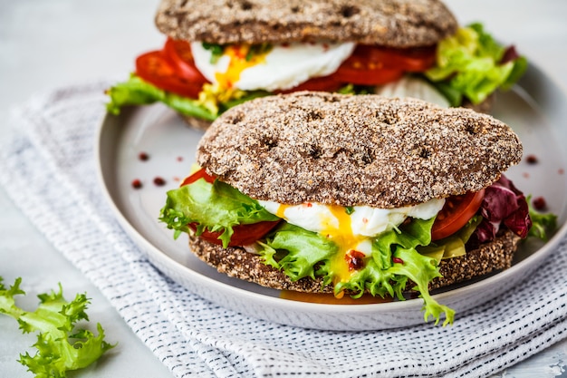 Sandwich de huevo escalfado con pan de centeno y tomate en placa gris.