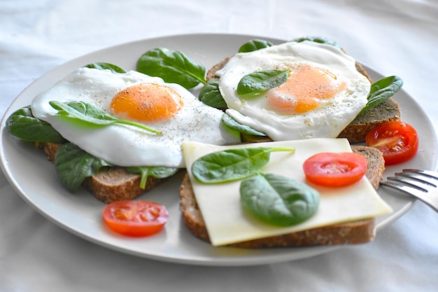 Sándwich de huevo con queso, tomates cherry y espinacas con pan integral en un plato blanco