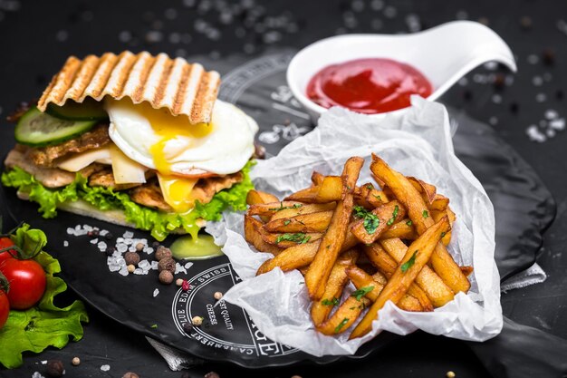 sándwich con huevos, carnes y hierbas, queso, papas fritas o adajo, salsa en un tazón blanco, un plato de