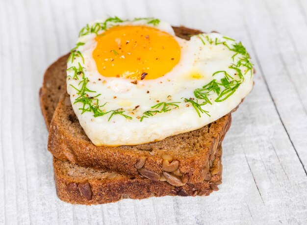 Sandwich con huevos fritos en forma de corazón sobre un fondo de madera