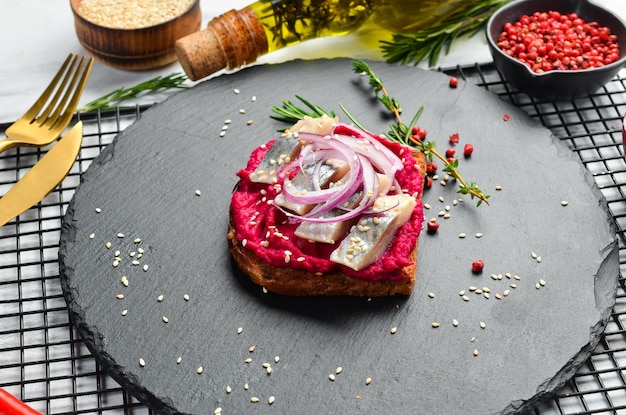 Sándwich con hummus de remolacha, arenque y cebolla Desayuno En un plato de piedra negra